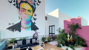 A modern outdoor seating area with a mural, a pink wall, and a wooden deck. - DOCA 201 by Tripintravel (Playa del Carmen)