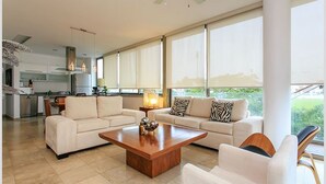 A spacious living room with a large coffee table, two sofas, and a view of the kitchen and outdoors. - DOCA 203 by Tripintravel (Playa del Carmen)