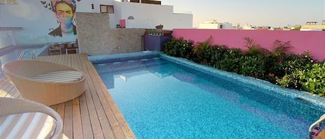 A rooftop pool with a wooden deck, a mural, and a pink wall.