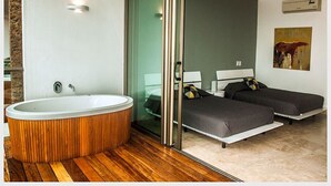 A modern bathroom with a freestanding bathtub, a glass shower enclosure, and a separate bedroom with two beds and a ceiling fan.