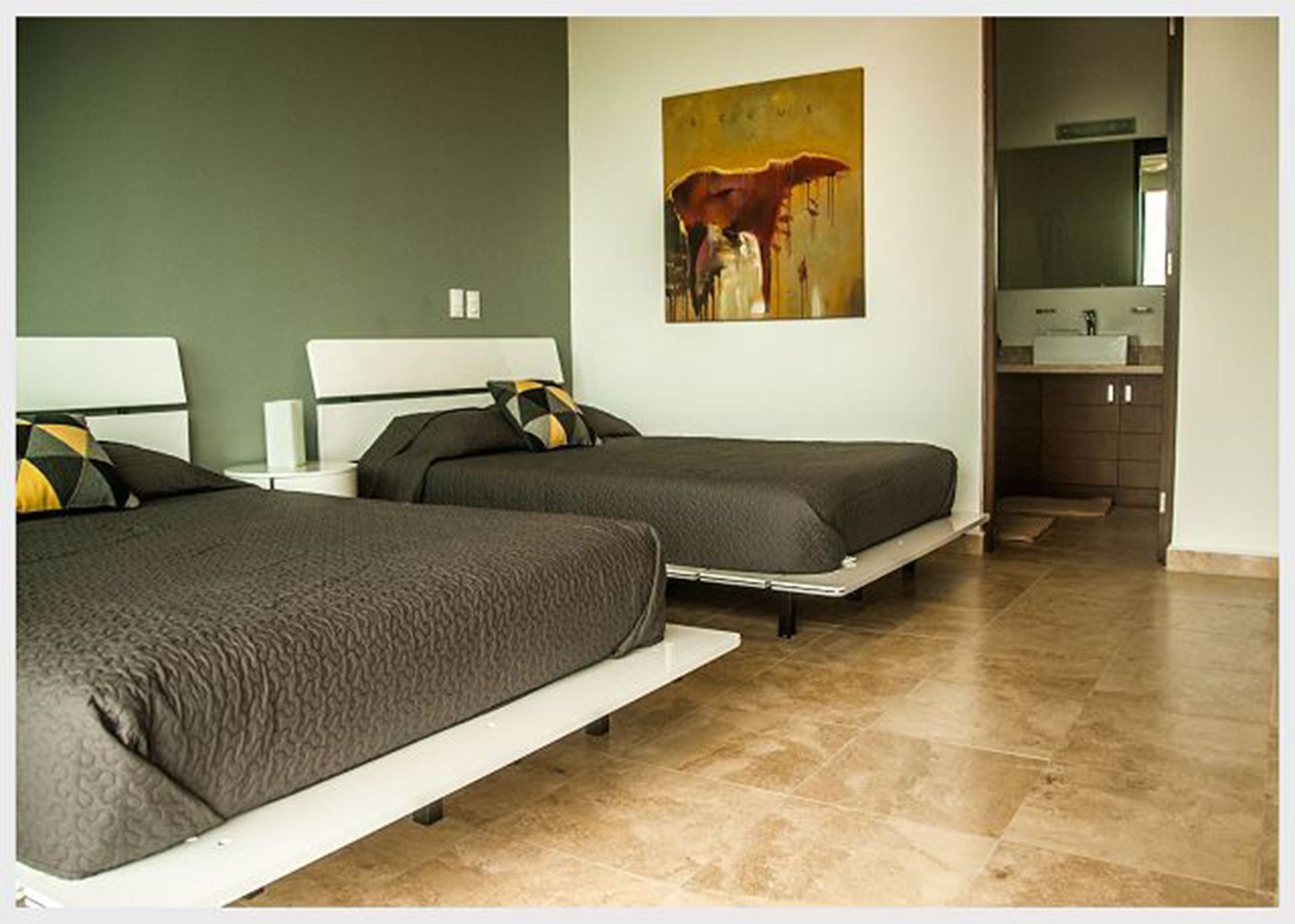 A hotel room with two beds, a painting on the wall, and a bathroom visible through an open door.