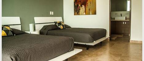A hotel room with two beds, a painting on the wall, and a bathroom visible through an open door.