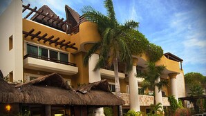 A hotel with a thatched-roof restaurant, palm trees, and a multi-story building with balconies. - Pueblito Luxury Penthouse by Tripintravel (Playa del Carmen)