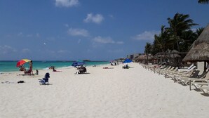 A beach with white sand, palm trees, and beach umbrellas. There are lounge chairs and a few people on the beach. - Pueblito Luxury Penthouse by Tripintravel (Playa del Carmen)