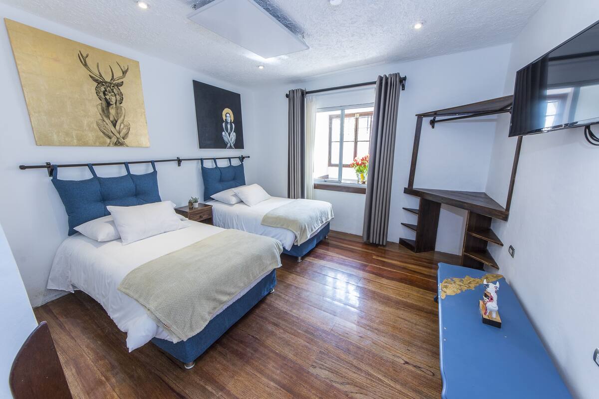 A bedroom with two beds, a TV, and artwork on the walls.