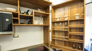 Una cucina con forno a microonde integrato, mensole in legno con stoviglie e una sedia blu.