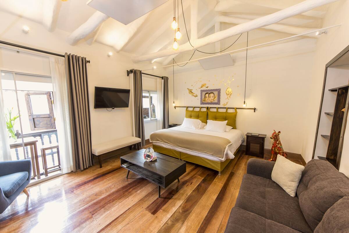A modern hotel room with a bed, a sofa, a coffee table, and a TV.