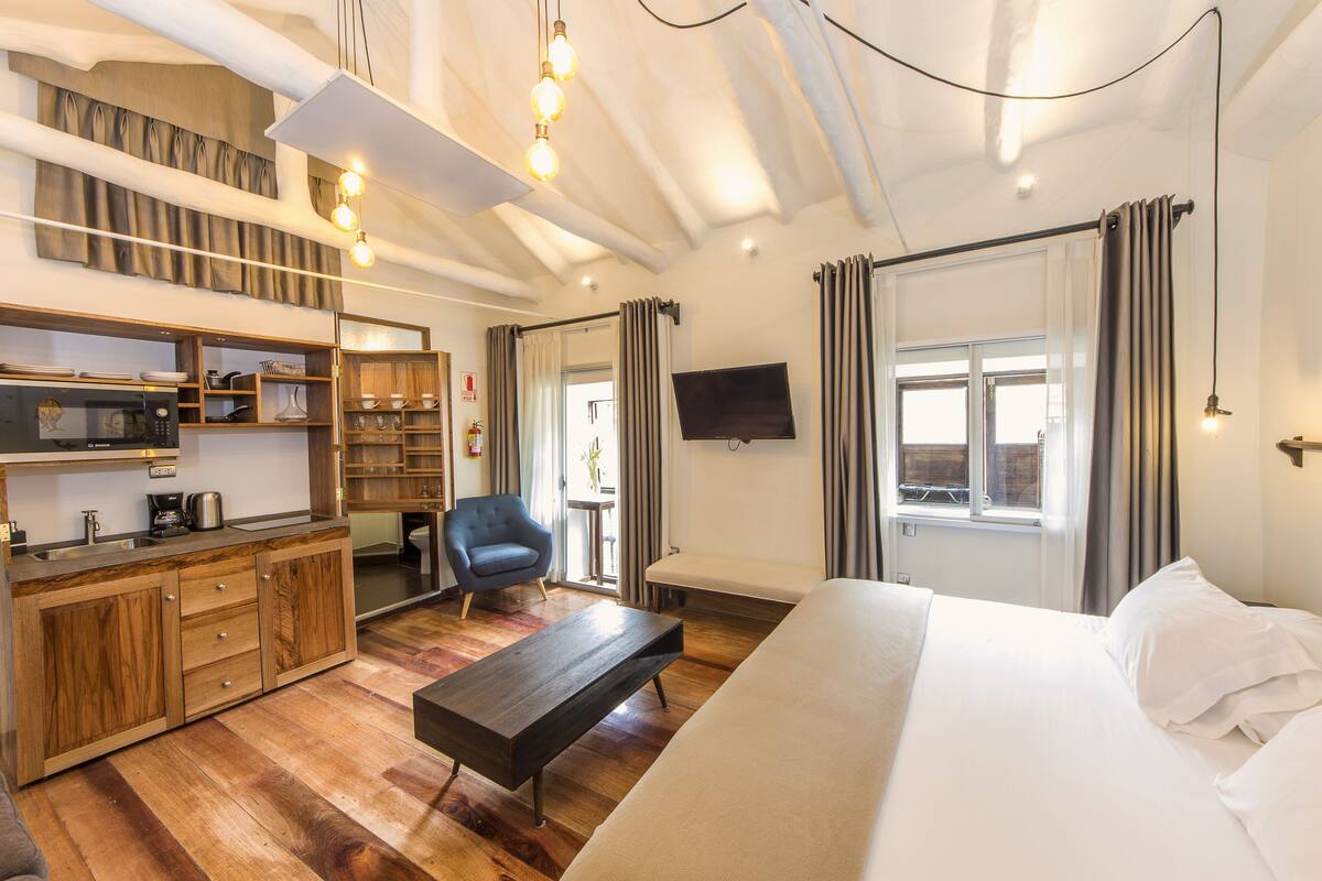 A modern hotel room with a wooden floor, a bed, a desk with a chair, a TV, and a window with curtains.