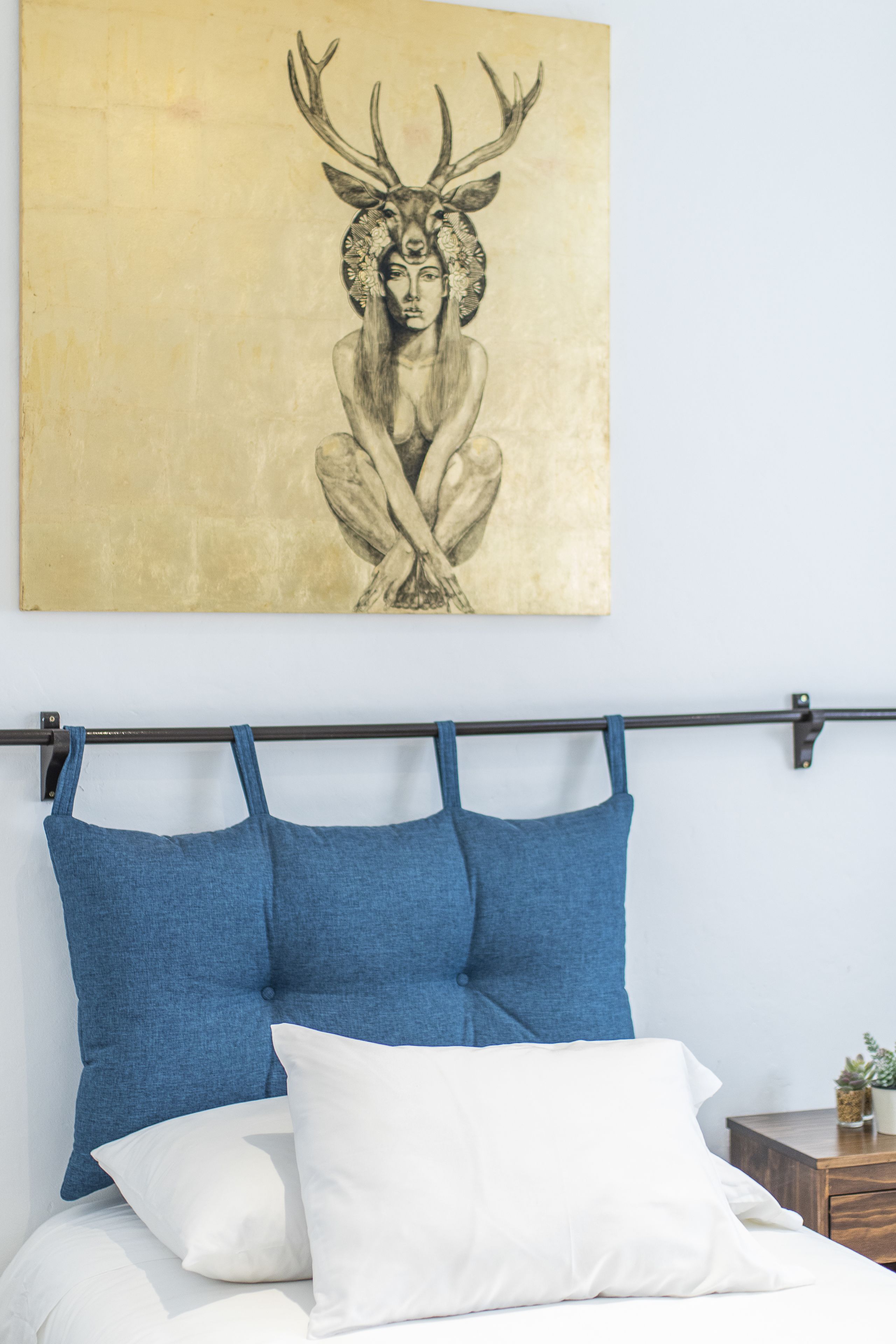 A bed with a headboard, blue and white pillows, and a wall-mounted artwork.