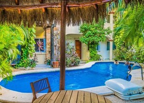 A pool area with a thatched roof, surrounded by lush greenery and a small building with a door and windows. - Magic, 1 block from Mamitas Beach by Tripintravel (Playa del Carmen)