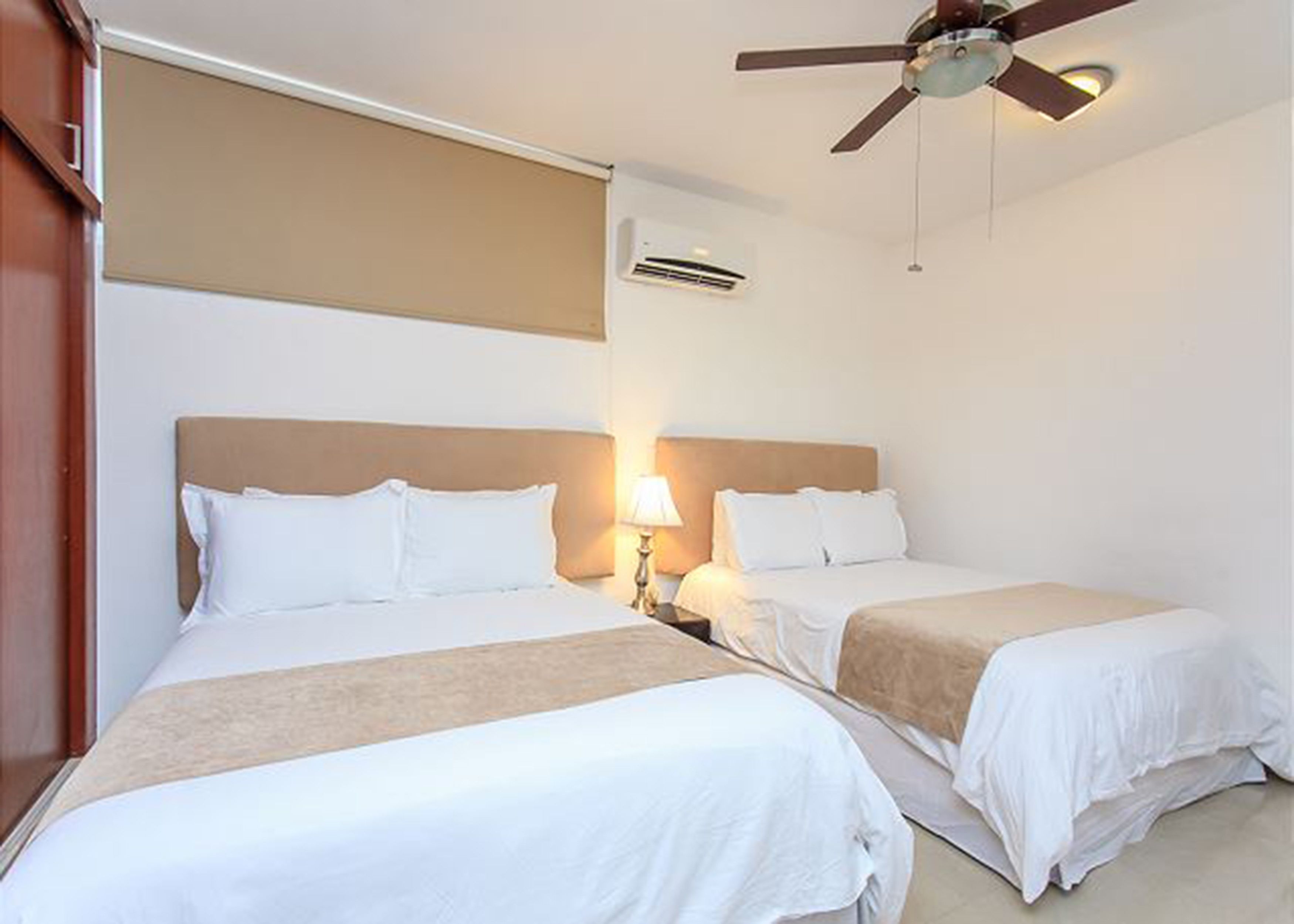 Een hotelkamer met twee bedden, een plafondventilator, een airconditioningsunit en een bedlampje.
