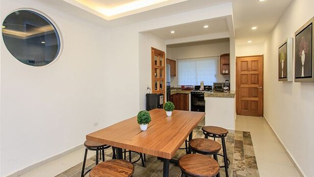 Une cuisine moderne avec des meubles en bois, un îlot central et un coin repas comprenant une table et des tabourets en bois.