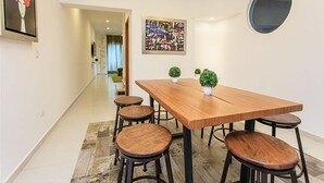 Ein moderner Essbereich mit einem Holztisch, vier Hocker, einem runden Spiegel an der Wand und zwei kleinen Topfpflanzen.