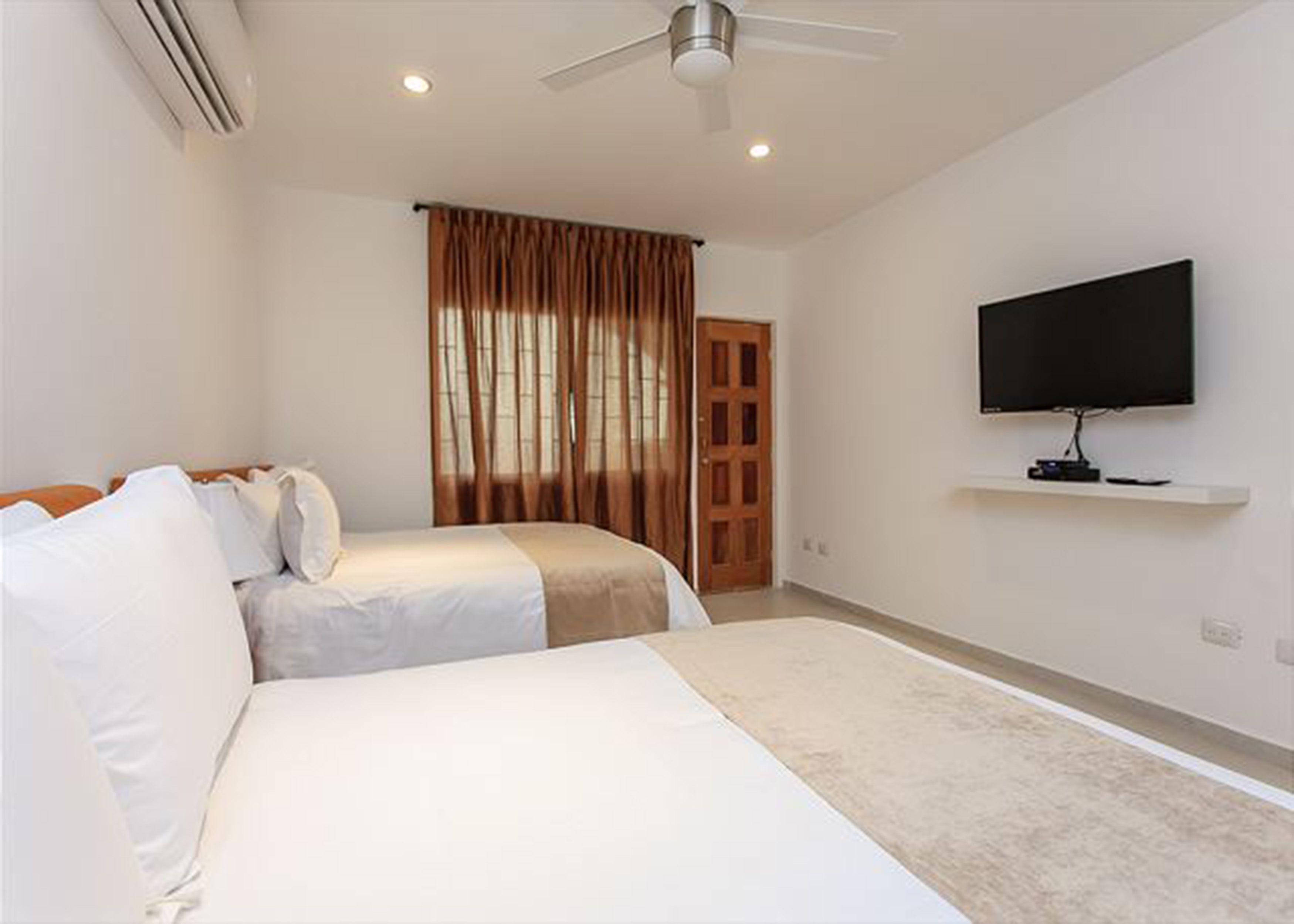 Ein Schlafzimmer mit zwei Betten, einem Deckenventilator, einem Fernseher auf einem Regal und einer Tür zu einem anderen Raum.