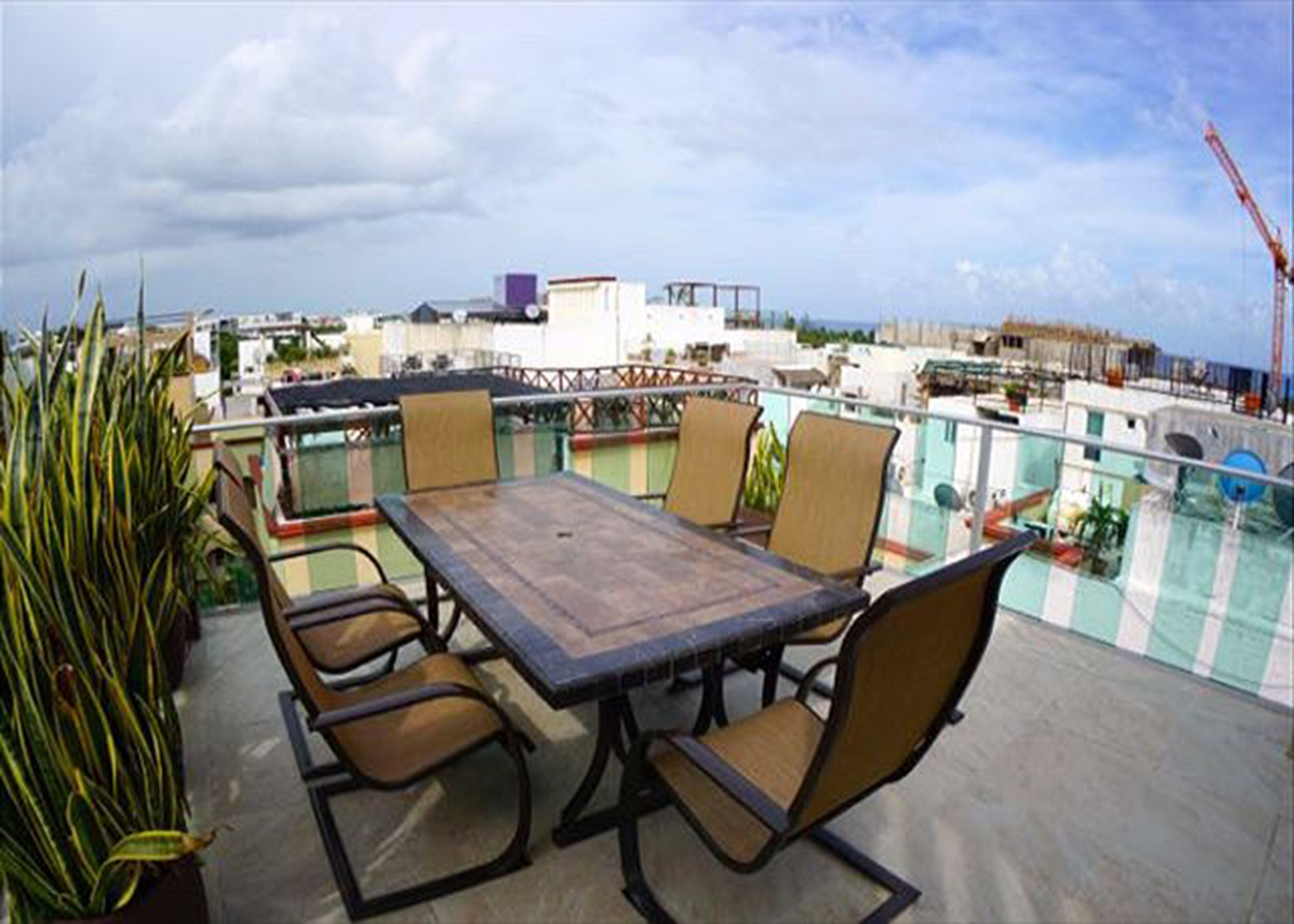 Terraço no telhado com mesa e cadeiras de madeira, cercado por plantas em vasos.