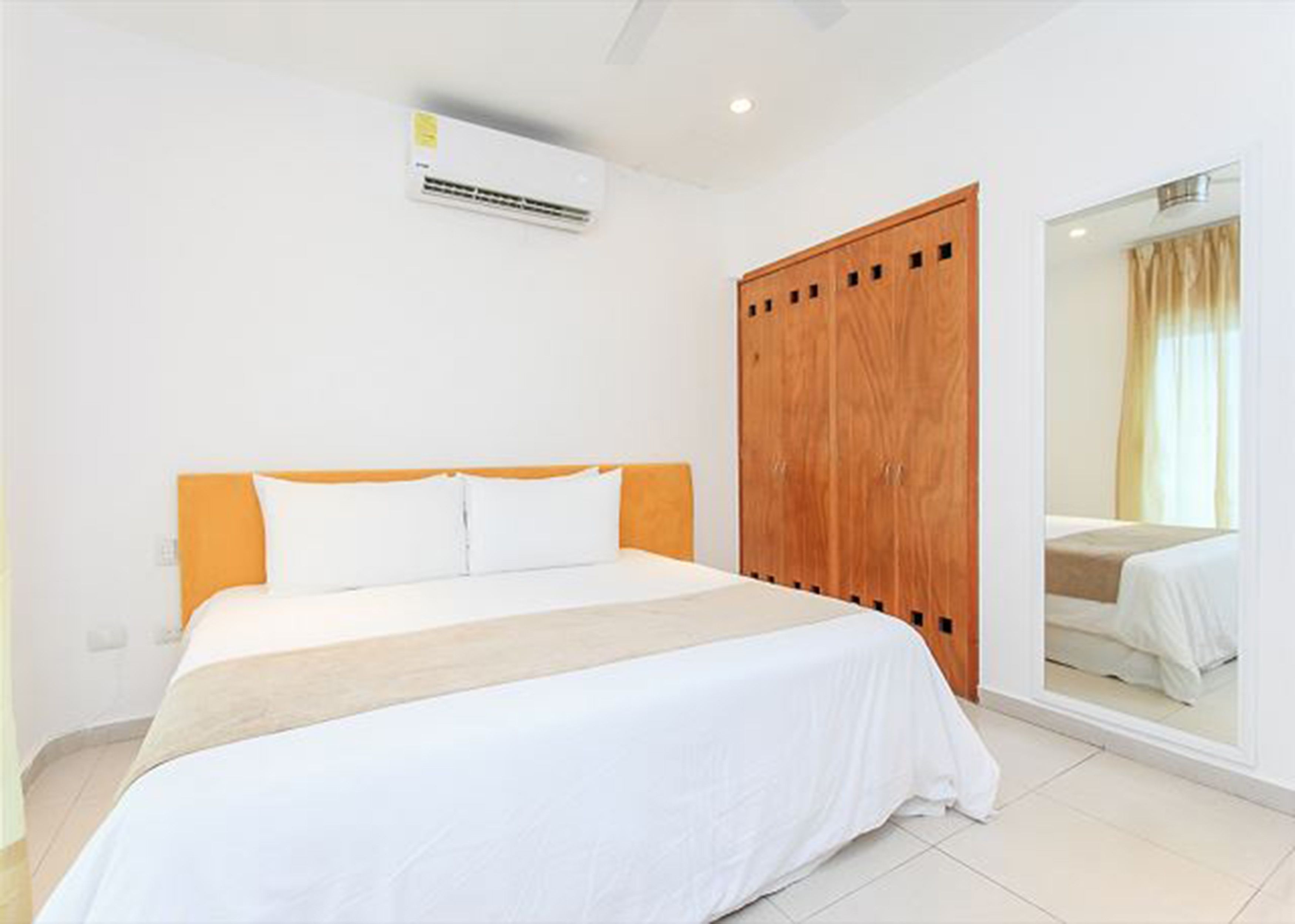 A bedroom with a bed, a wooden wardrobe, and a mirror on the wall.