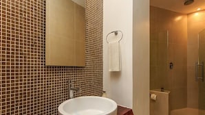 Un baño con lavamanos blanco, espejo y zona de ducha.