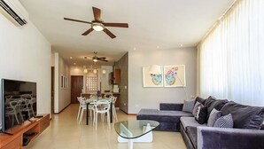 Una sala moderna con sofá, una mesa de centro de vidrio, una zona de comedor con sillas y ventiladores de techo.