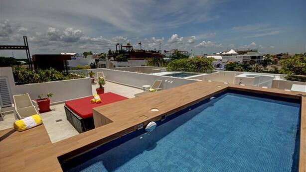 A rooftop pool with a wooden deck, red lounge area, and a clear view of the city skyline. - Nolita 22 by Tripintravel (Playa del Carmen)