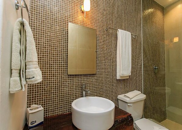 A bathroom with a tiled wall, a sink, a toilet, and a shower area.