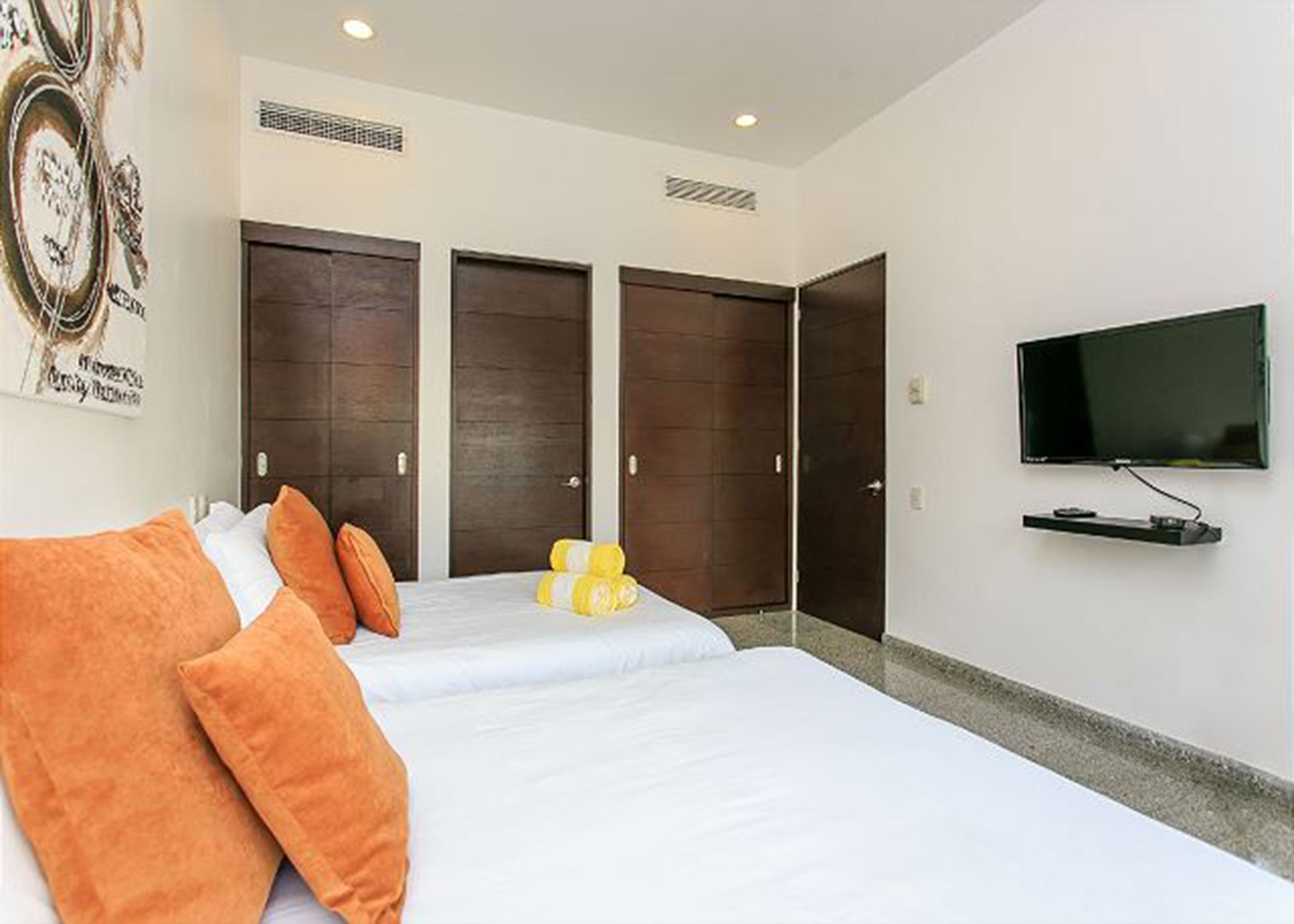 A hotel room with two beds, a flat-screen TV, and a wall-mounted TV.