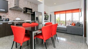 A modern kitchen with a dining area, a large window with an orange blind, and a grey sofa in the living room. - Infinito 03 by Tripintravel (Playa del Carmen)
