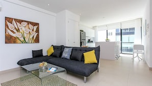 Ein modernes Wohnzimmer mit einem dunkelgrauen Sofa, einem Glastisch und einem Blumenbild an der Wand.