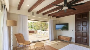 A bedroom with a large bed, a ceiling fan, a TV, and a sliding glass door leading to an outdoor area with a table and chairs. - Oceanfront Exclusive Home (Playa del Carmen)