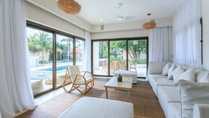 A modern hotel room with a large sliding glass door to a pool, a sofa, a chair, and a small table. - Oceanfront Exclusive Home (Playa del Carmen)