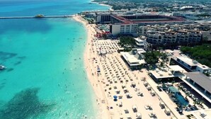An aerial view of a beach resort with a long sandy beach, a pool area, and several buildings with balconies overlooking the beach. - Oceanfront Exclusive Home (Playa del Carmen)