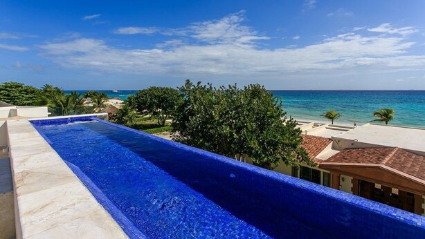 A long, narrow swimming pool with a clear view of the ocean and palm trees in the background. - Oceanfront Exclusive Home (Playa del Carmen)