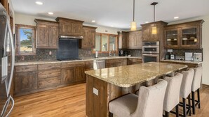 Una cocina amplia con armarios de madera, encimeras de granito y una isla central con taburetes de bar.