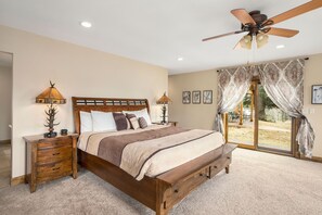 Une chambre à coucher avec un lit en bois, deux tables de chevet, un ventilateur de plafond et une grande fenêtre avec des rideaux.