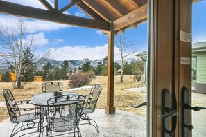 Une terrasse couverte avec une table ronde et des chaises, une pergola en bois et une vue sur les montagnes et les arbres.