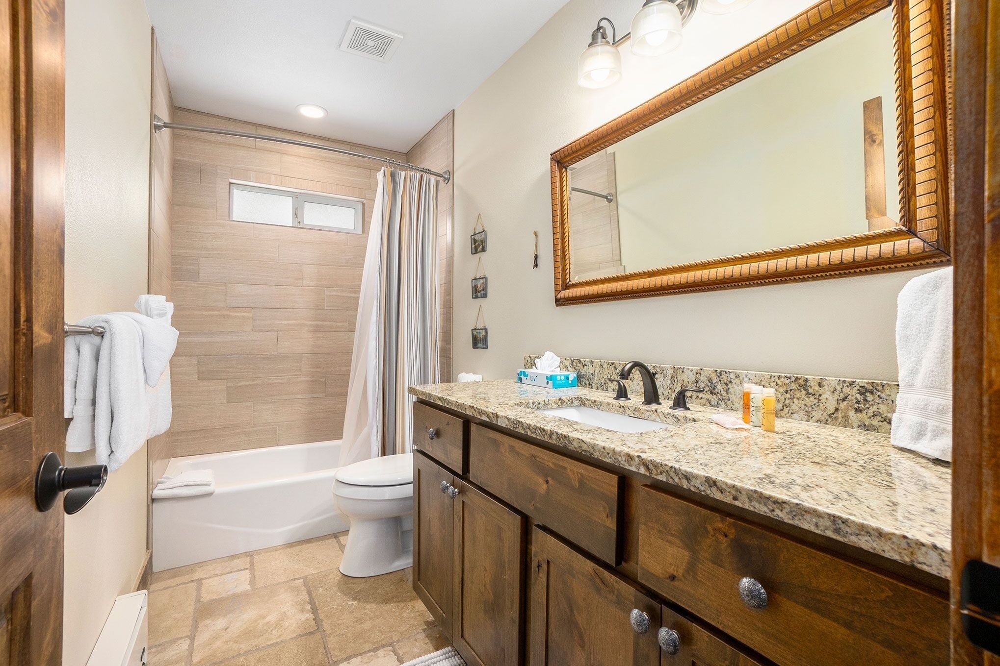 A bathroom with a wooden vanity, a large mirror, a shower area, and a toilet.