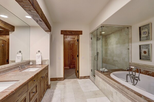 A modern bathroom with a large mirror, two sinks, a walk-in shower, and a bathtub.