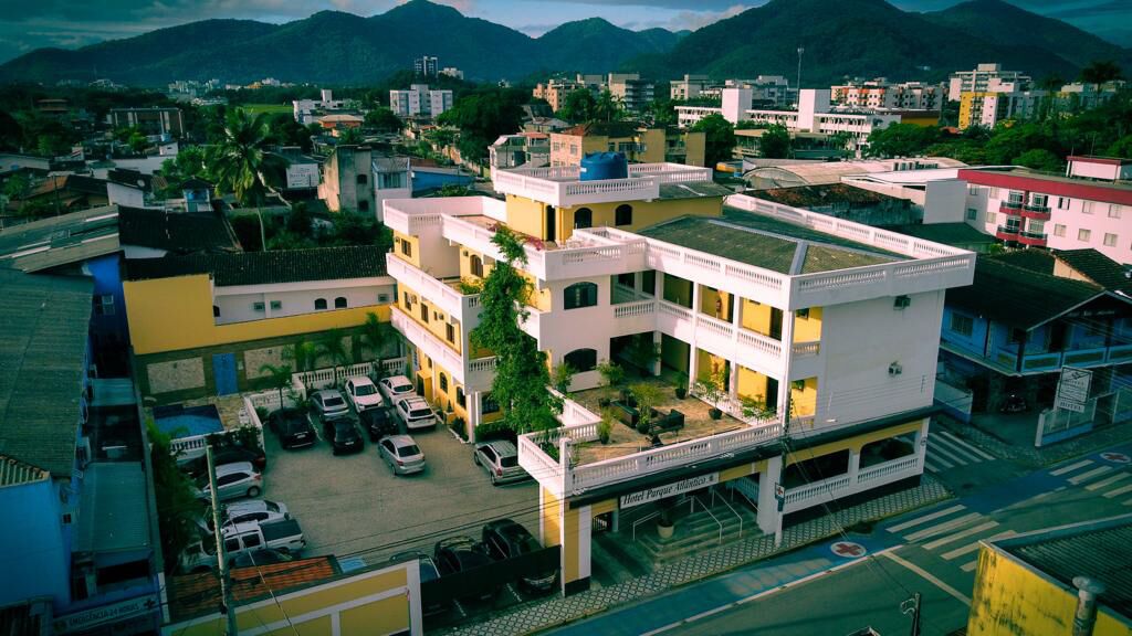 A multi-story hotel with a central courtyard, parking area, and a view of surrounding buildings and mountains.