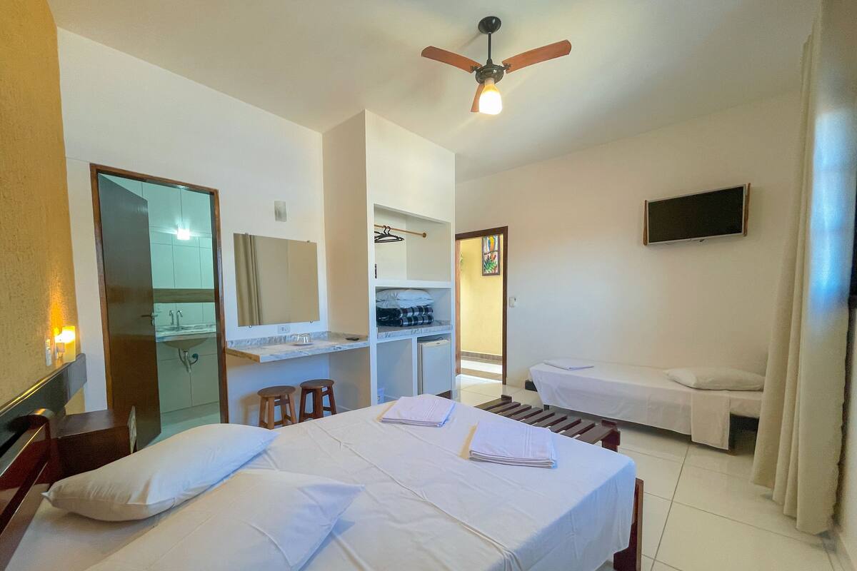 Habitación de hotel con cama, escritorio con silla, televisor y baño con espejo y lavabo.
