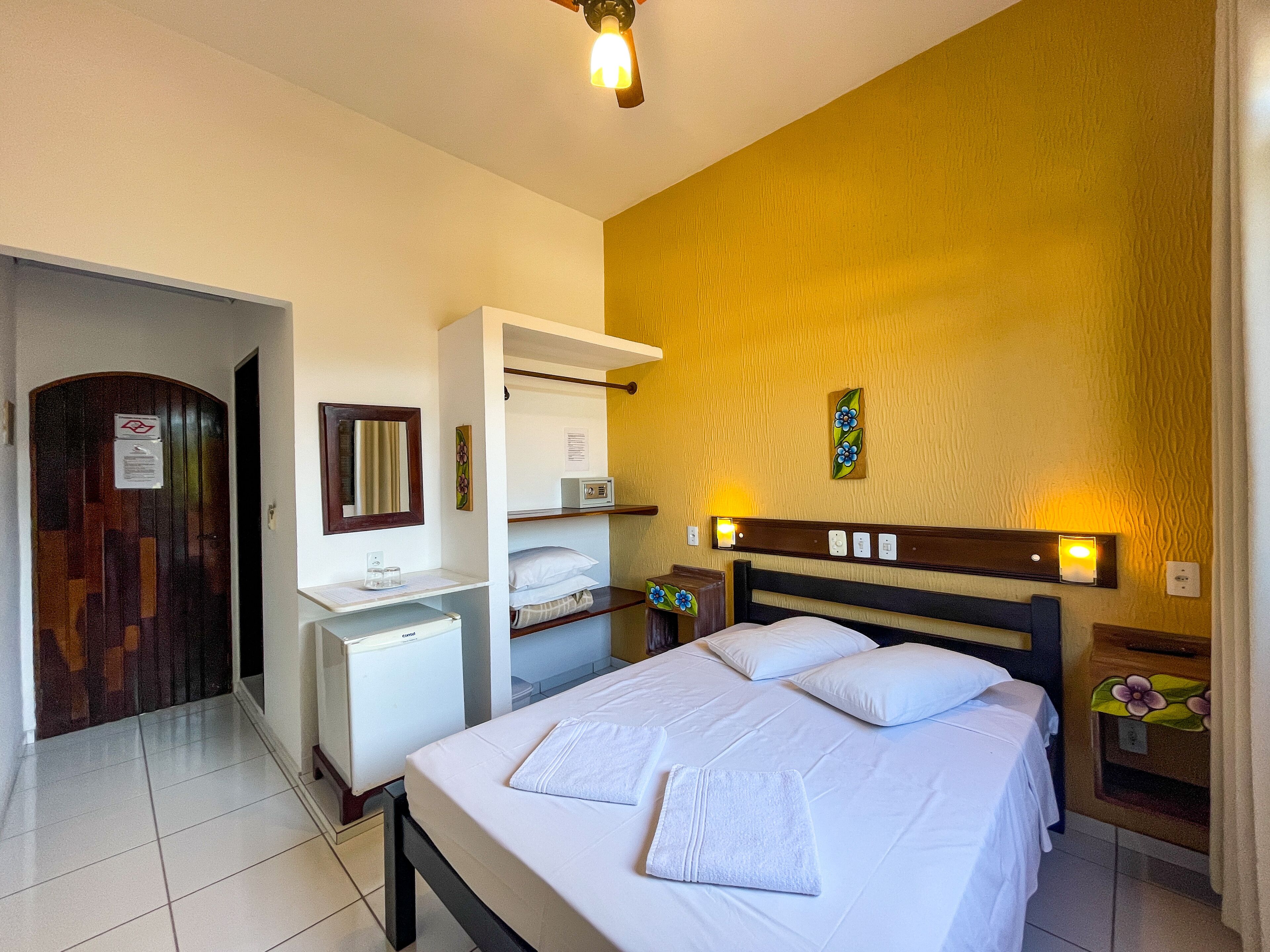A hotel room with a bed, bedside tables, a wardrobe, and a small desk with a mirror.