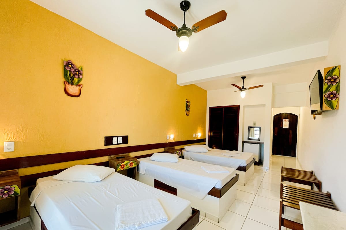 Habitación de hotel con tres camas, un ventilador de techo, un televisor y un escritorio pequeño.