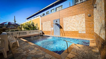 Ein Pool mit Steinfliesen, einem weißen Zaun und einem blauen Gebäude im Hintergrund.