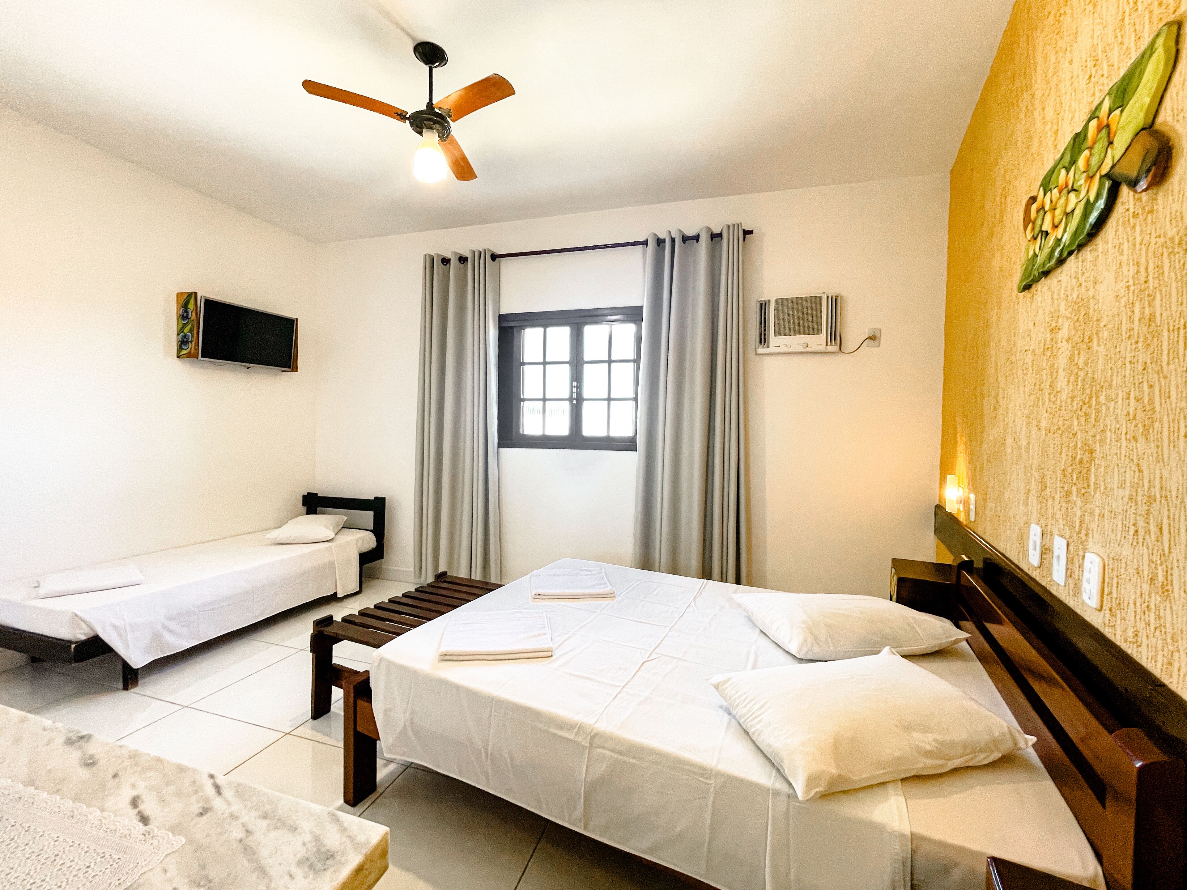 Habitación de hotel con dos camas individuales, ventilador de techo, televisión, equipo de aire acondicionado y ventana con cortinas.