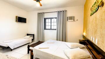 Habitación de hotel con dos camas individuales, ventilador de techo, televisión, equipo de aire acondicionado y ventana con cortinas.