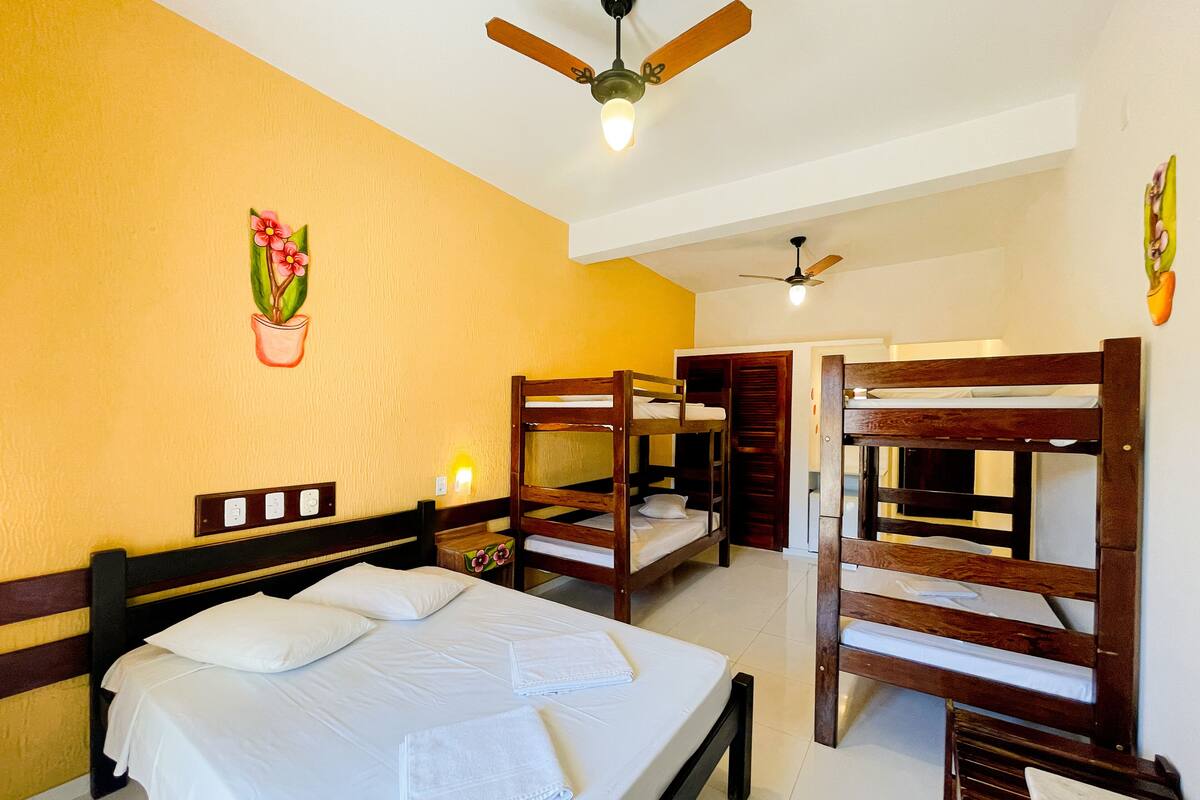 Habitación de hotel con literas, ventilador de techo e iluminación fijada a la pared.