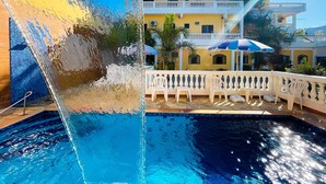 A swimming pool with a water fountain, a white fence, and a building with balconies in the background. - Parque Atlântico Hotel (Ubatuba)
