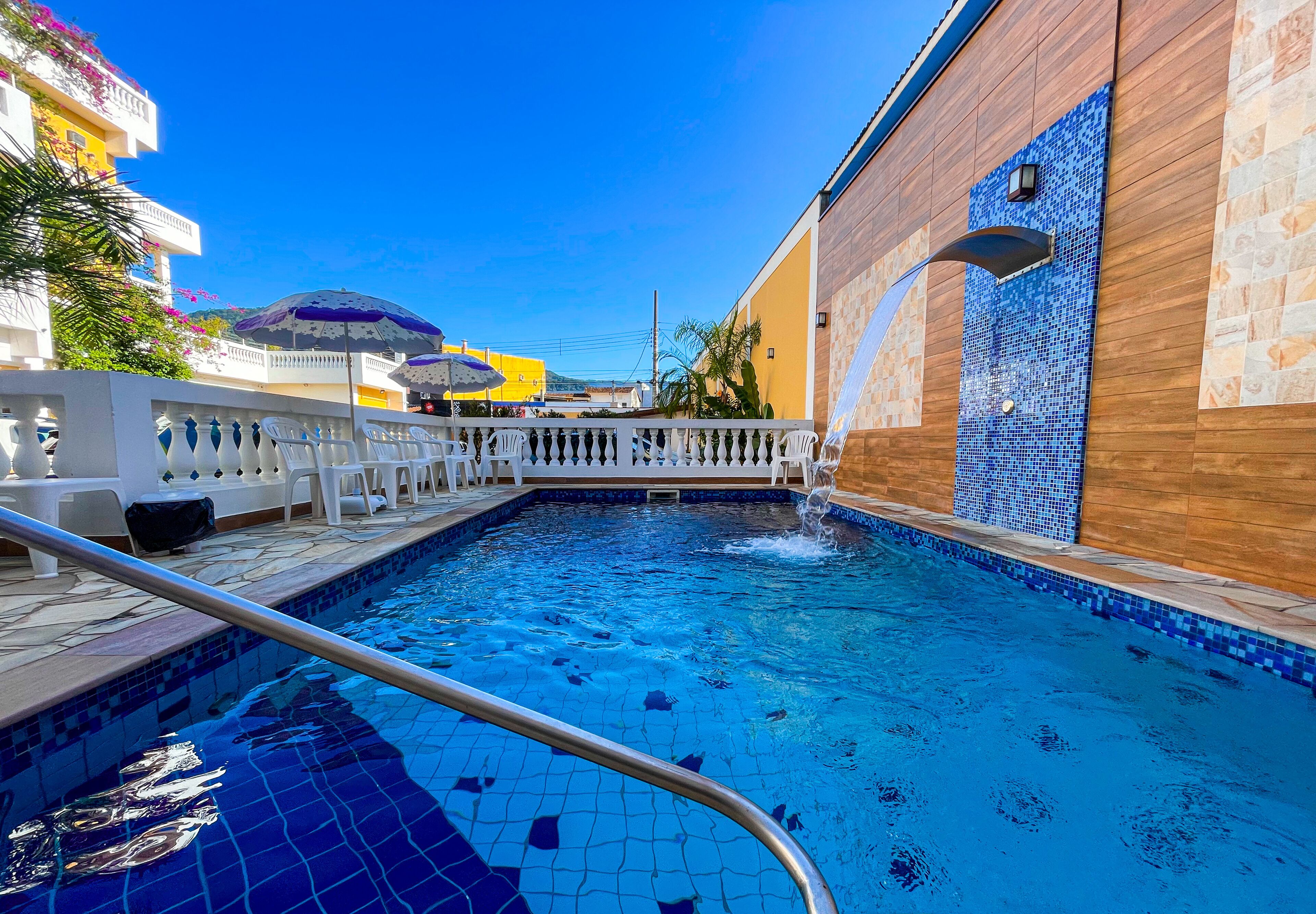 Una piscina con borde de azulejos, valla blanca y un edificio con muro de mosaicos.