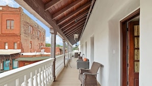 A covered porch with a white balustrade, wicker furniture, and a view of a red brick building. - National Hotel Jackson, Tapestry Collection by Hilton (Jackson)