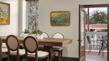 Een eetruimte met een houten tafel en stoelen, een potplant en twee ingelijste schilderijen aan de muur.