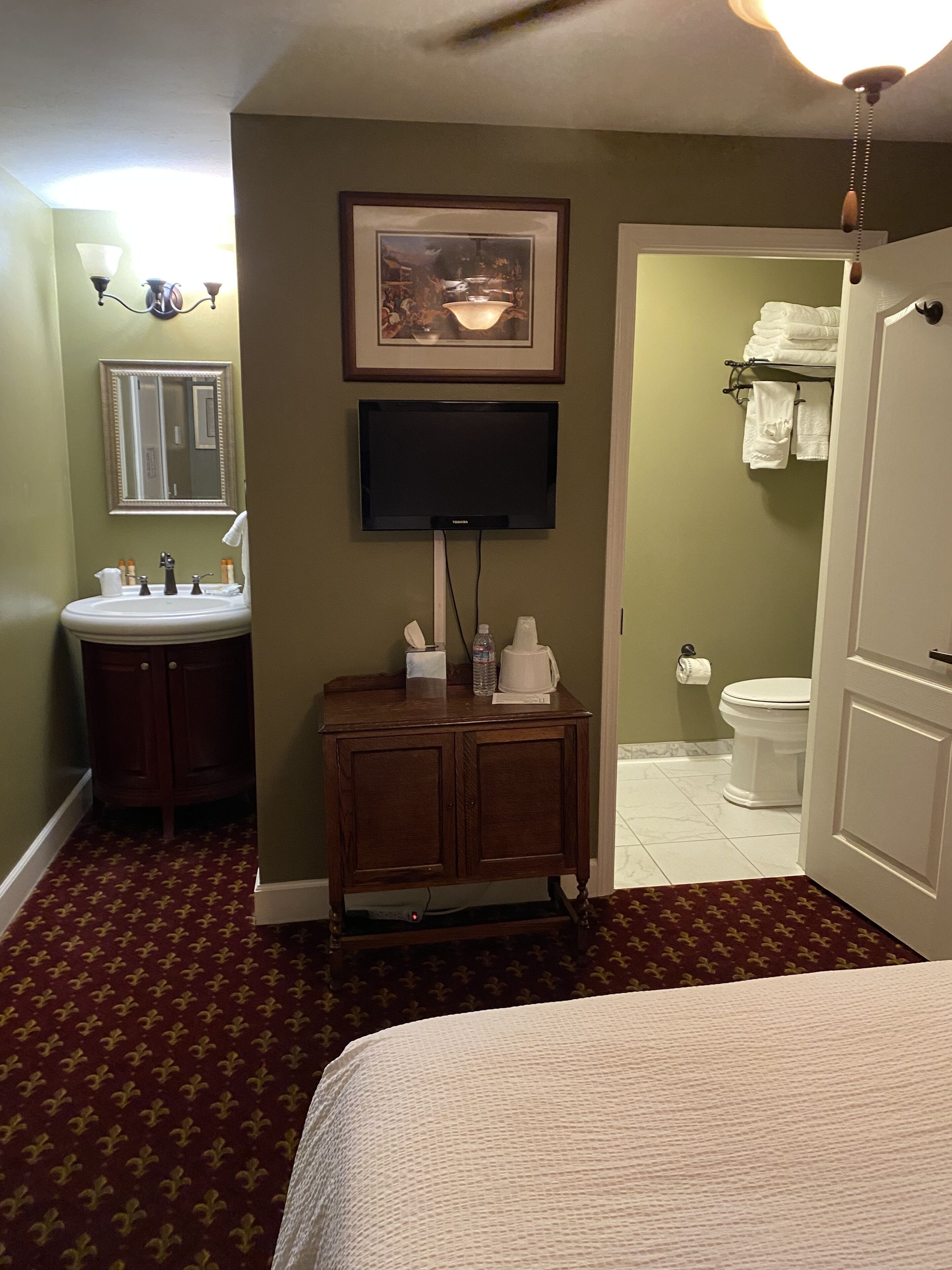 Une salle de bain d’hôtel équipée d’un lavabo, d’un miroir, d’une œuvre d’art encadrée et de toilettes.