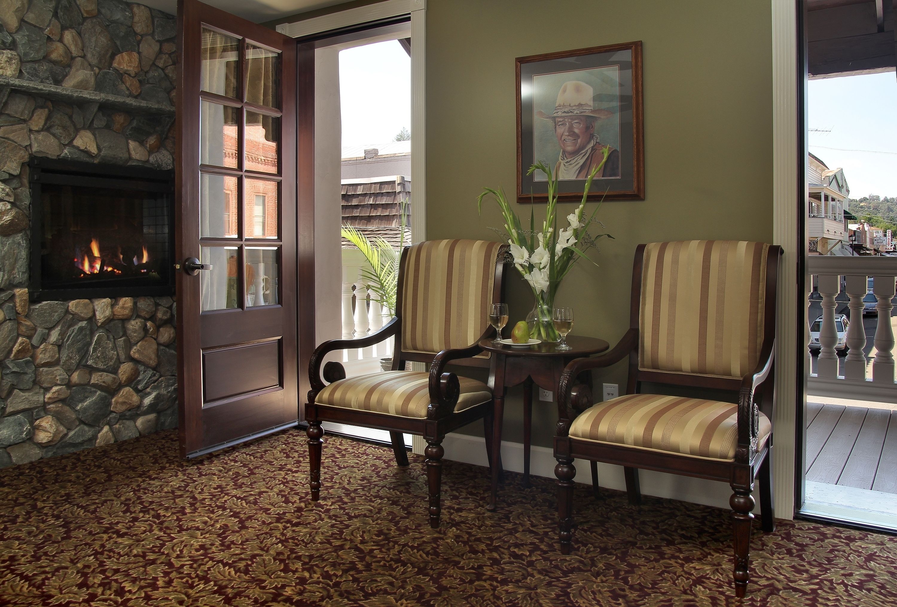 A room with a stone fireplace, two striped chairs, a table with a vase, and a door leading outside.
